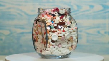 Mavimsi bir arka planda çeşitli haplarla dolu büyük bir cam kavanoz dönüyor. Covid-19 Coronavirüs enfeksiyonundan tedavi arayışı konsepti.