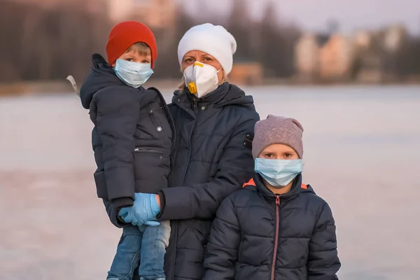 Mother, son and daughter in medical masks on the lake in the Park. Protection against coronavirus infections Covid-19.