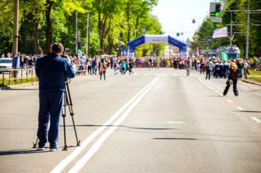Spor takım elbiseli operatör maratonun başındaki videoyu çekiyor.