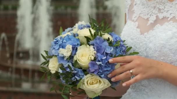 白いドレスの花嫁は噴水の背景を背景にバラの結婚式の花束を調節し 滑ります 閉じろ — ストック動画