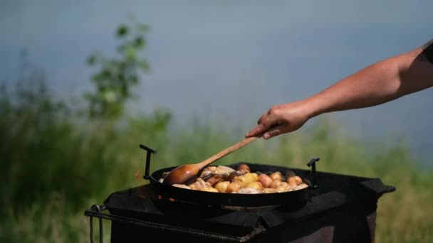 蓋をしてディスクからフライパンを揚げ 直火で調理する 料理人は若い揚げジャガイモを攪拌するために木製のスプーンを使用します — ストック動画