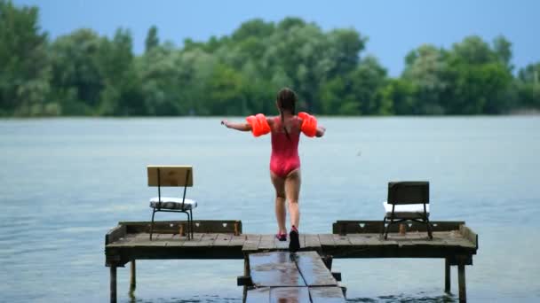 少女は夏の日に木の桟橋から水の中に飛び込みます 新鮮な空気の中で滞在 スローモーション — ストック動画
