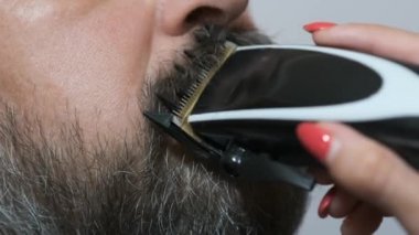 Karantina sırasında mutfakta elektrikli makasla kocasının bıyığını kesen bir kadın. Sosyal mesafeye uyum. Sosyal tecrit kavramı.