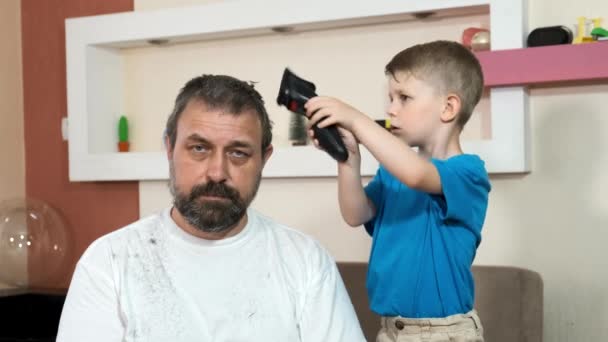 小さな男の子が電気ヘアクリッパーで父親の頭の上の髪を切ります 隔離中の自己分離 — ストック動画