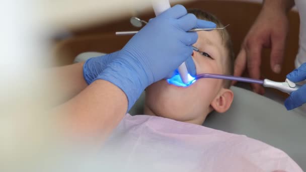 一个小男孩坐在牙科诊所的椅子上 女牙医戴着防护手套 把牙齿封住 健康的概念 — 图库视频影像