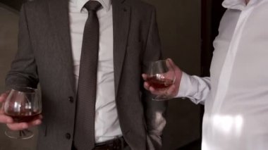 Ceketli ve gömlekli iki adam viski bardaklarını yakın plan çekimle tokuşturuyor. Yavaş çekim.