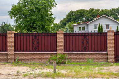 Tuğla sütunlu ve bukleli kırmızı metal çitler. Profilli metalin dokusu.