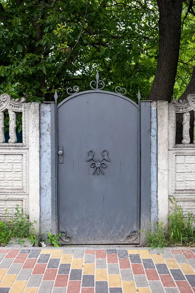 Decorative, gray, old metal gate between the white concrete slabs of the fence.