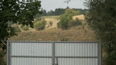 Rüzgarda sallanan tarlaların ve ağaçların arka planına karşı kıvrımlı demir kapılar..