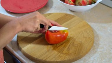 Kadının elleri mutfak bıçağıyla ahşap kesim tahtasına biber şeklinde domates kesiyor. Sağlıklı beslenme. Mutfakta Sebze Pişirme. 