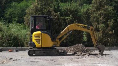 Küçük sarı bir kazıcı yeşil ağaçların arka planına karşı bir çukur kazıyor..