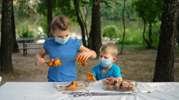 男の子と女の子は串焼きにマリネした肉を入れます 公園のピクニックで医療用マスクの子供たち Covid 19パンデミック時の屋外レクリエーション — ストック動画