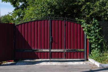 Yeşil bahçenin etrafında kırmızı metal çitler var. Profilli metalin dokusu.