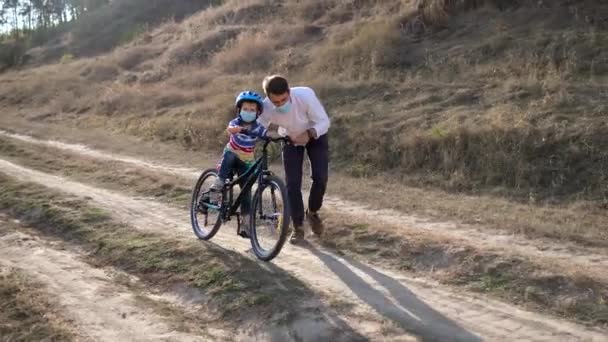 Joven Padre Enseña Hijo Montar Bicicleta Con Máscaras Médicas Casco — Vídeos de Stock
