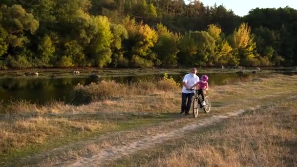 髭を生やした父親は 娘に医療用マスクと川の近くの自転車用ヘルメットに乗ることを教えています — ストック動画