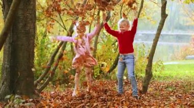İki küçük kız parka sonbahar yaprakları fırlatıyor. Sonbahar Parkı 'nda oynayan çocuk. Düşen yapraklar. Sonbaharda açık hava eğlencesi.