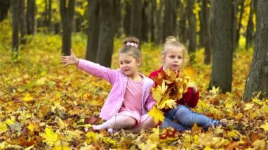 İki küçük kız, sonbaharda parkta bir buket sarı yaprak topluyor..