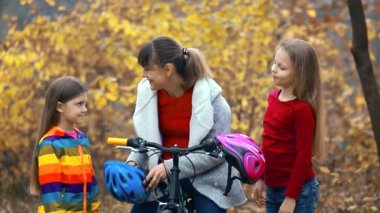 Anne, sonbahar günü doğada bisiklet sürmeden önce iki kızın kaskını takmasına yardım eder ve birbirlerine beş tane verir. Güvenlik, spor, eğlence.