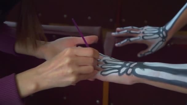Mamá pinta las manos de la niña con pintura blanca y negra. La huella del esqueleto en el cuerpo. preparándose para Halloween. — Vídeos de Stock