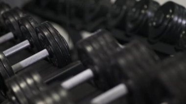 Bir adam spor salonunda ağır dambılları elleriyle alır. Kapat..
