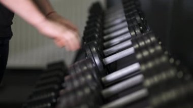 Bir adam spor salonunda ağır dambılları elleriyle alır. Kapat..