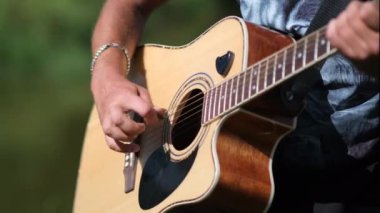 Genç adam doğanın arka planında gitar çalar. Kapat..
