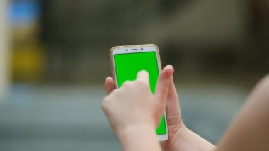 Kızın eli yeşil ekranlı akıllı telefonu tutuyor. Arka plan görüntüsü. Chroma anahtarı, kızın elini dikey yeşil ekranla kapat..