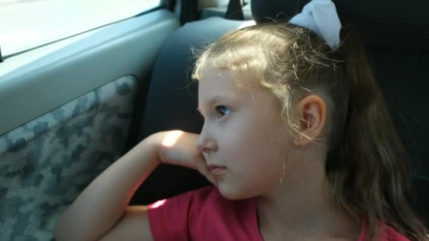 女の子が車に乗って窓の外を見ている 窓の外には町の木や家が点滅した — ストック動画