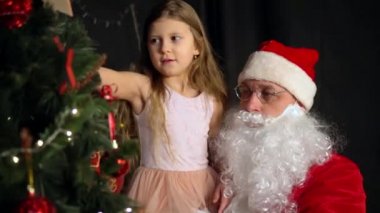 Noel Baba ve küçük bir kız Noel ağacı süsler. Noel Baba kızı kollarına aldı ve büyük kırmızı bir top astı..