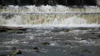 Güneşli bir günde küçük bir baraj manzarası. Suyun aktığı küçük bir baraj. Köpüklü çizgiler ve desenler olarak görülüyor. Yavaş çekim 100fps