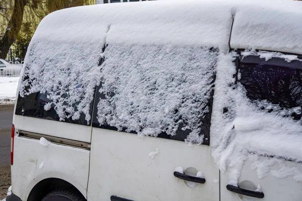 Donmuş araba, kış günü karla kaplı beyaz minivan. Kar fırtınasında şehir hayatının şehir manzarası.