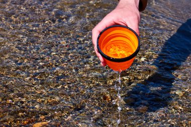 Erkek turist bulanık nehirlerin arka plan karşı bir katlanır fincan taşıyan , Bir adam bir dağ dere su topluyor