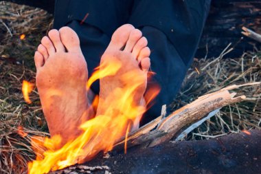 kamp ateşe yakın borefoot , Adam ateş üzerinde çıplak ayaklarını ısıtır