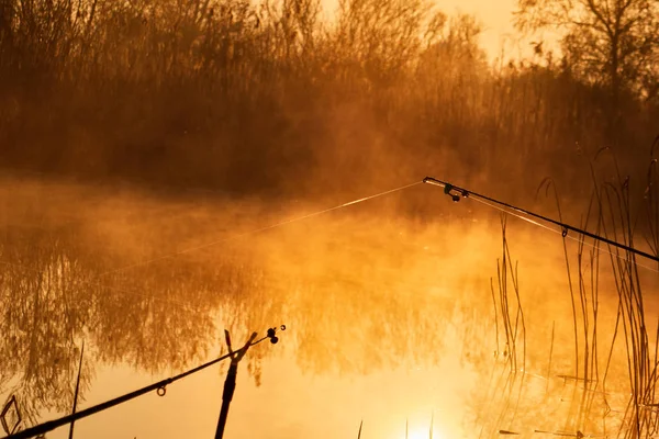 Angelrute aus nächster Nähe bei nebligem Sonnenaufgang über dem See, Sonnenaufgang über dem See spiegelt sich auf der Wasseroberfläche — Stockfoto