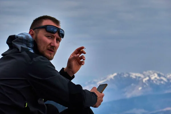 Το αγόρι καπνίζει και κρατά το τηλέφωνο στα βουνά με φόντο μια όμορφη θέα — Φωτογραφία Αρχείου