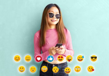 Cep telefonunda emoji yazan Asyalı bir kız. Genç Asyalı bir kadın güneş gözlüğü takıyor ve yeşil arka planda izole edilmiş cep telefonundan mesaj gönderiyor.