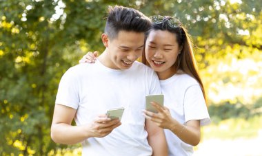 Genç çift güneşli bir günde şehir parkında akıllı telefon kullanıyor. Gezici teknoloji kullanarak boş zamanlarını birlikte geçiriyorlar.