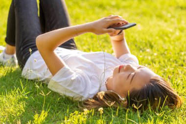 Elinde akıllı telefonla gülümseyen kız zafer işareti gösteriyor ve parmakları V ile dilek diliyor.