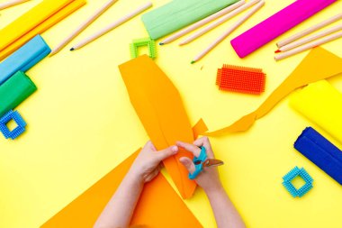 Çocuk, makasıyla renkli turuncu kağıtları makasla kesiyor.