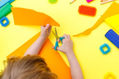 Çocuk, makasıyla renkli turuncu kağıtları makasla kesiyor.