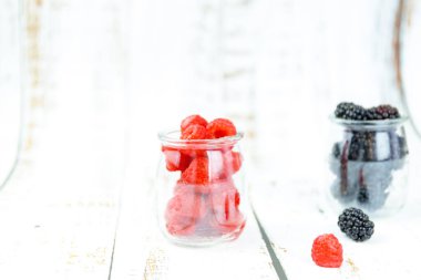 Bahçe meyveleri, ahududu ve bektaşi üzümlü cam şişeler içinde ahşap arka planda. Sağlıklı gıda konsepti. Okul defterleri için resim.