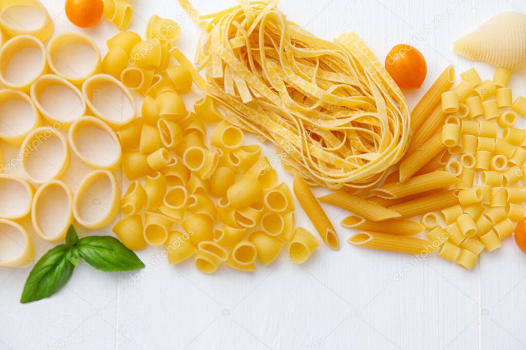 Various uncooked pasta on white wooden background. Top view. Italian pasta for restaurant with space for text.