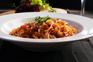 Siyah bir peçetenin üzerinde beyaz bir tabakta spagetti.