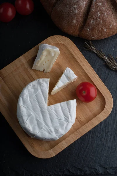 Fromage de Brie français frais et une tranche sur une planche de bambou avec tomates cerises, pain sur la plaque noire. vue de dessus. — Photo