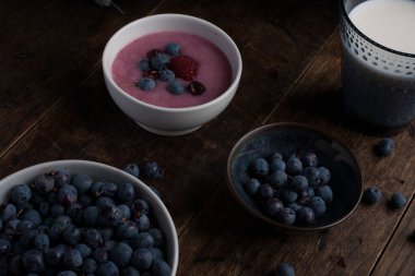 Bir bardak süt, bir fincan yaban mersini, bir fincan yoğurt ve eski ahşap masanın üzerinde devedikeni dalı. Kahvaltı.