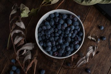 Eski ahşap masada bir kase yaban mersini ve kurumuş dallar. Düz yatıyordu