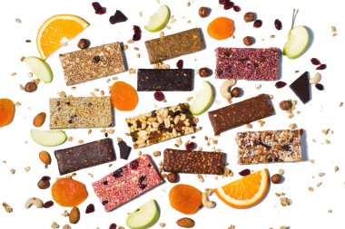 Tahıl gevreği, fındıklı protein barları ve beyaz arka planda kuru meyve meyveleri ve farklı malzemelerle bezenmiş düz bir bileşim.