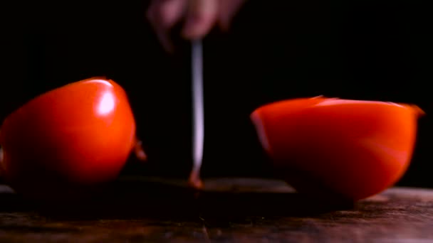 Skär den röda tomaten i två bitar. Skär tomat med vit keramisk kniv på en rustik träskiva. — Stockvideo