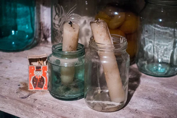 Two candles placed into small jars, and a box of matches on the shelf in cellar.