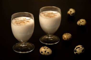 Şeffaf bir bardakta yumurta kokteyli, rendelenmiş hindistan cevizi serpiştirilmiş, bıldırcın yumurtalı siyah bir arka planda..